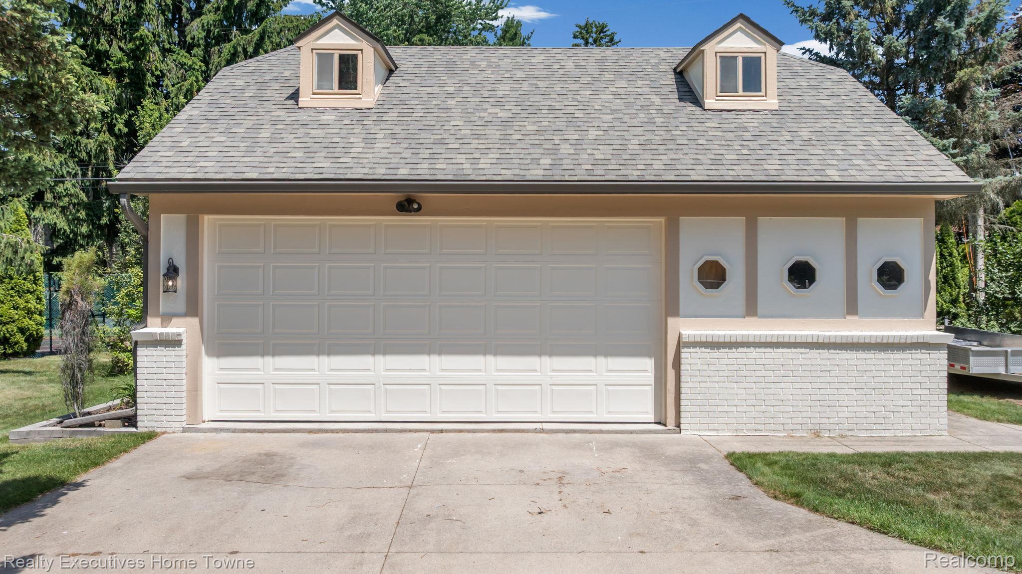 8308 Lakeshore Road Fort Gratiot, MI 48059 - Photo 3 of 79 Detached garage structure featuring a light-colored panel garage door, two dormer windows, a gray shingle roof, and white painted brick accents