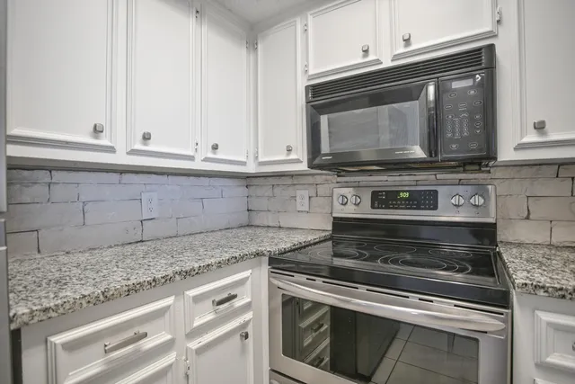 a kitchen with granite countertop white cabinets and a stove top oven