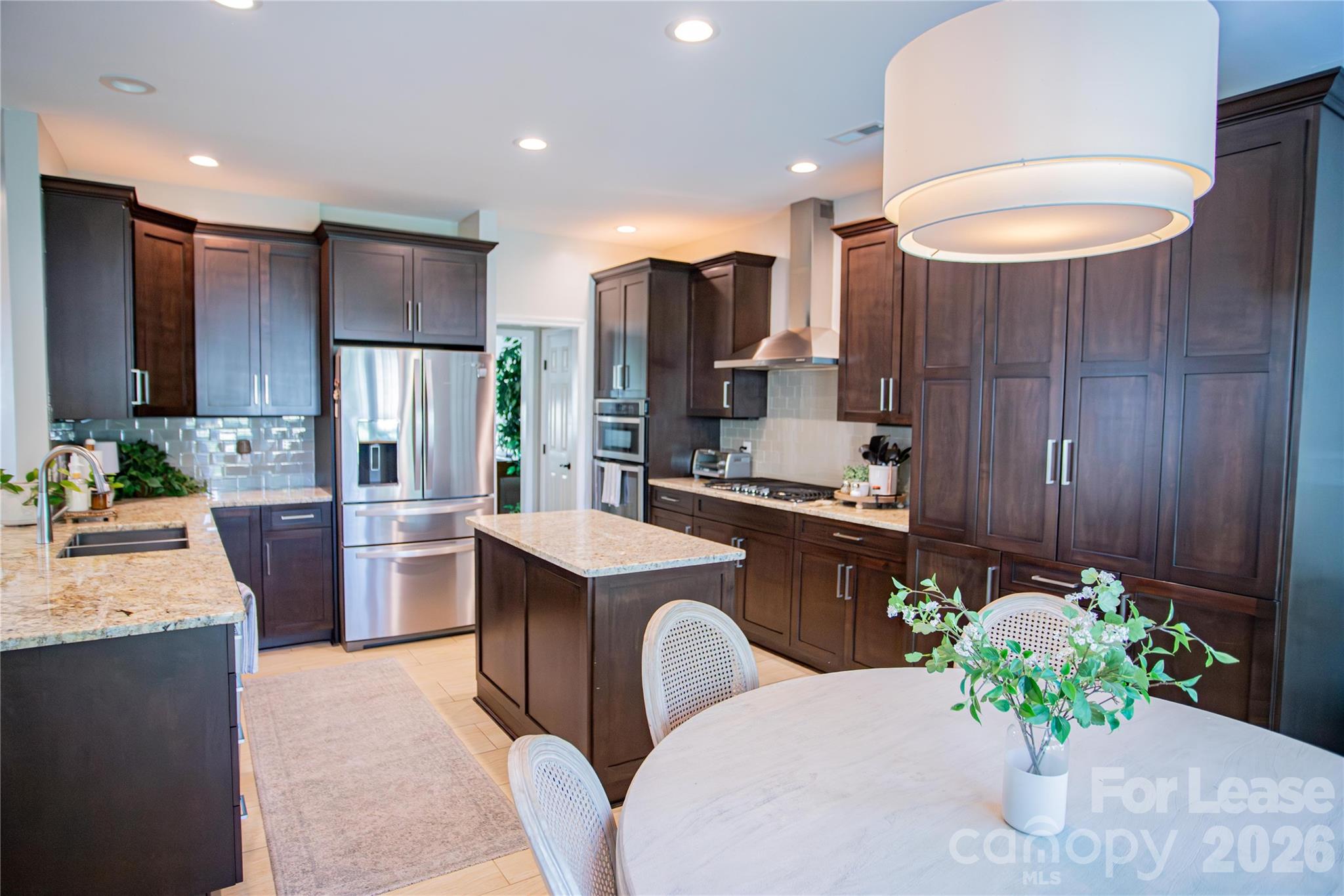 a kitchen with stainless steel appliances kitchen island granite countertop a refrigerator a sink a dining table and chairs