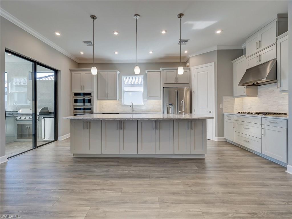 15107 Pescara Street Naples, FL 34114 - Photo 16 of 31 a large kitchen with stainless steel appliances kitchen island a large counter top a sink cabinets and a wooden floor