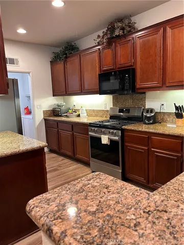 a kitchen with stainless steel appliances granite countertop a stove a sink dishwasher and a refrigerator with wooden cabinets