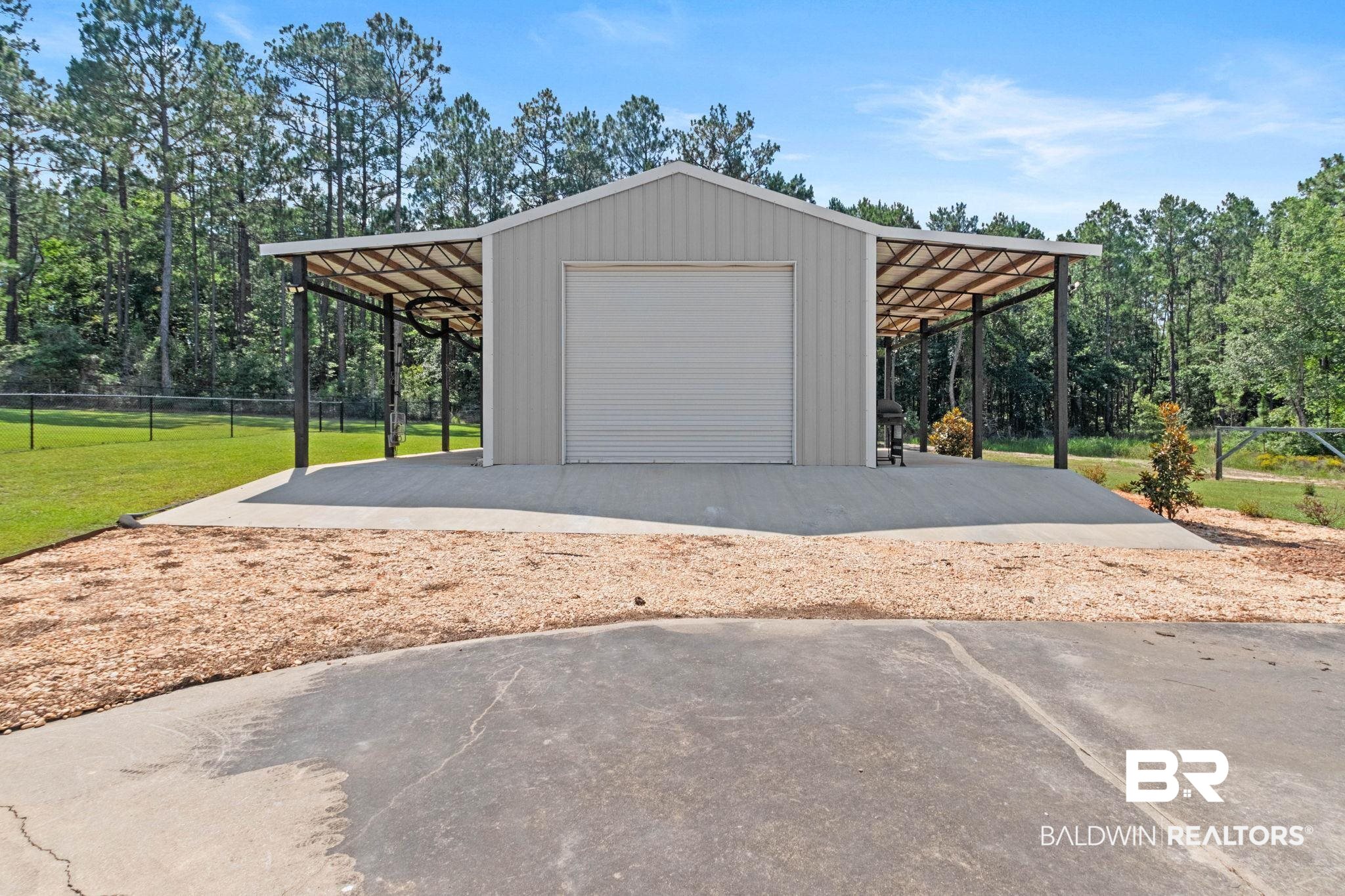 79 Whitetail Run Chatom, AL 36518 - Photo 75 of 82 Utility building featuring a roll-up door, expansive concrete pad, and covered side awnings with exposed structural framing