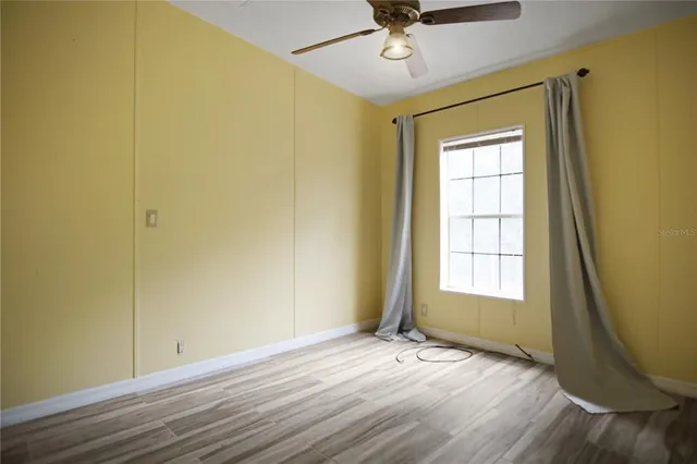 an empty room with wooden floor fan and windows