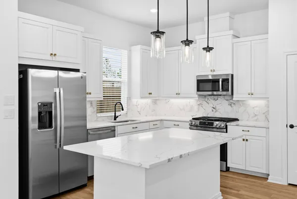 a kitchen with stainless steel appliances a refrigerator a sink a stove and white cabinets