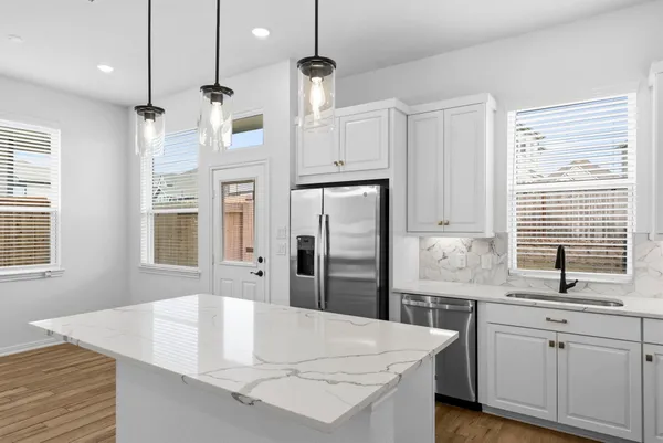 a large kitchen with stainless steel appliances kitchen island granite countertop a refrigerator a sink dishwasher a stove and white cabinets with wooden floor