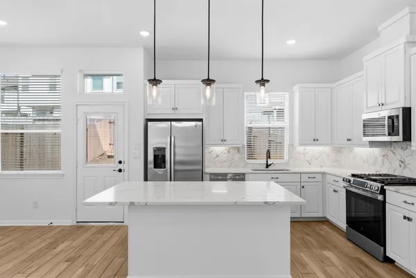 a kitchen with stainless steel appliances kitchen island granite countertop a stove a sink and white cabinets with wooden floor