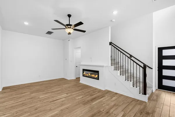 a view of a livingroom with wooden floor a ceiling fan and kitchen space