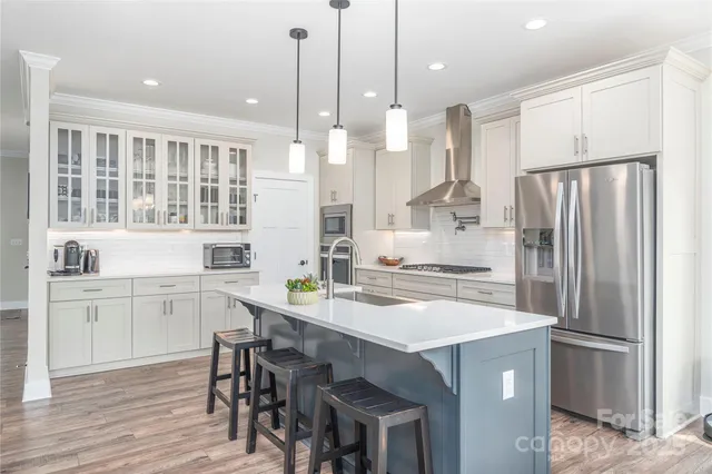 a kitchen with kitchen island a stove a refrigerator a sink and white cabinets with wooden floor