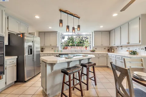 a kitchen with stainless steel appliances kitchen island granite countertop a table chairs sink refrigerator and cabinets