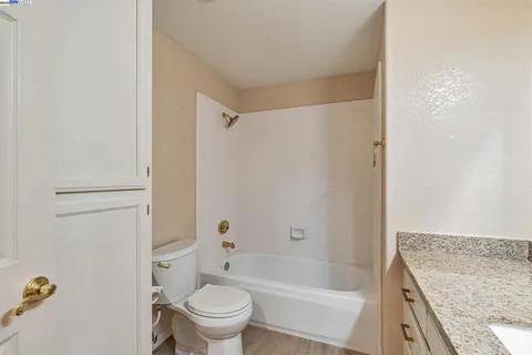 a bathroom with a granite countertop bathtub shower sink vanity and toilet