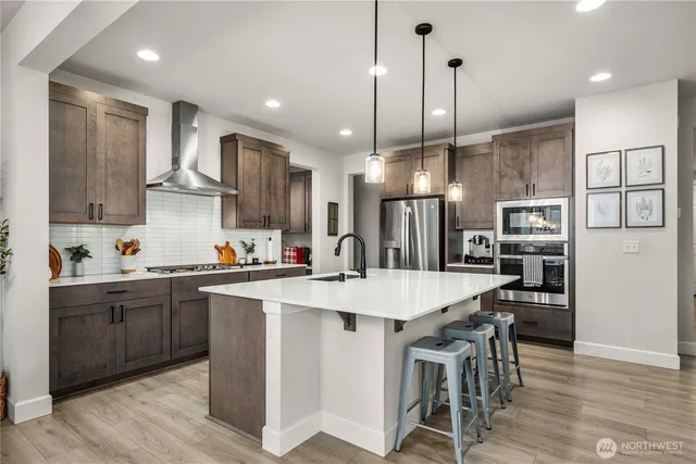 a kitchen with stainless steel appliances kitchen island granite countertop a sink a stove a refrigerator and island with wooden floor