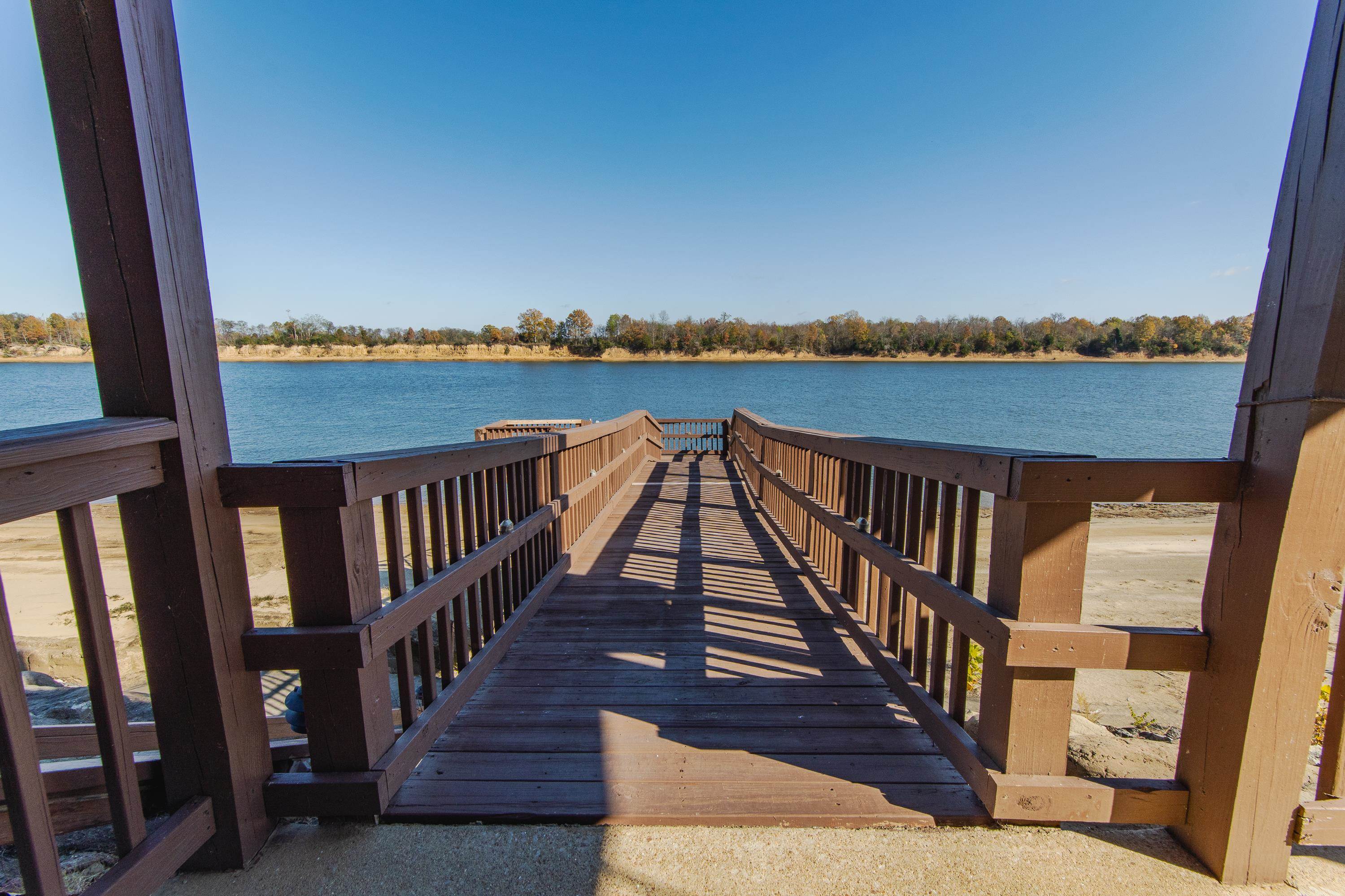 1111 Leaning Trees Lane Adamsville, TN 38310 - Photo 21 of 36 Wood-finish pier extending over a body of water, featuring sturdy railings, a clear blue sky, and a distant tree line