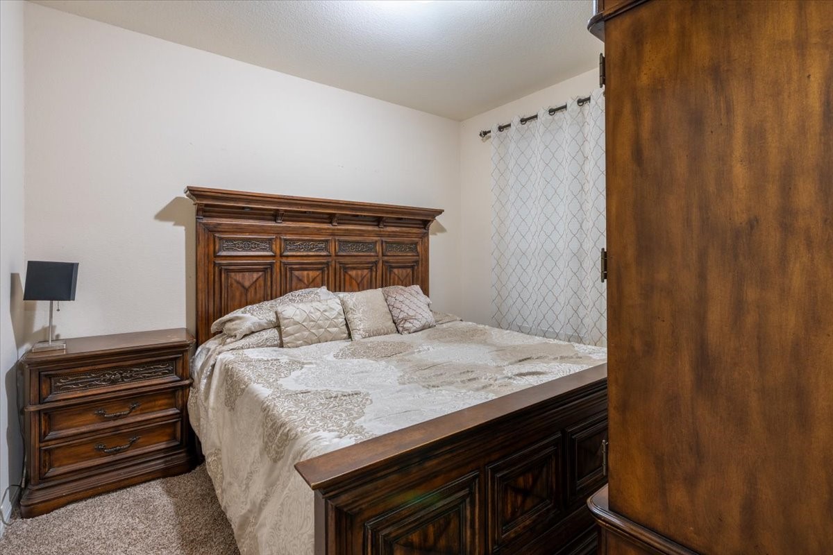22002 Flashing Ridge Spring, TX 77389 - Photo 12 of 43 Cozy bedroom featuring a large wooden bed with intricate detailing, matching nightstand, and soft, neutral-colored bedding. The room is warmly lit and has a patterned curtain adding elegance. Perfect for a restful retreat.