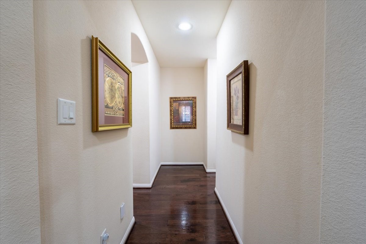 22002 Flashing Ridge Spring, TX 77389 - Photo 13 of 43 This photo showcases a well-lit hallway with elegant dark wood flooring and neutral walls adorned with framed artwork, creating a warm and inviting entrance.