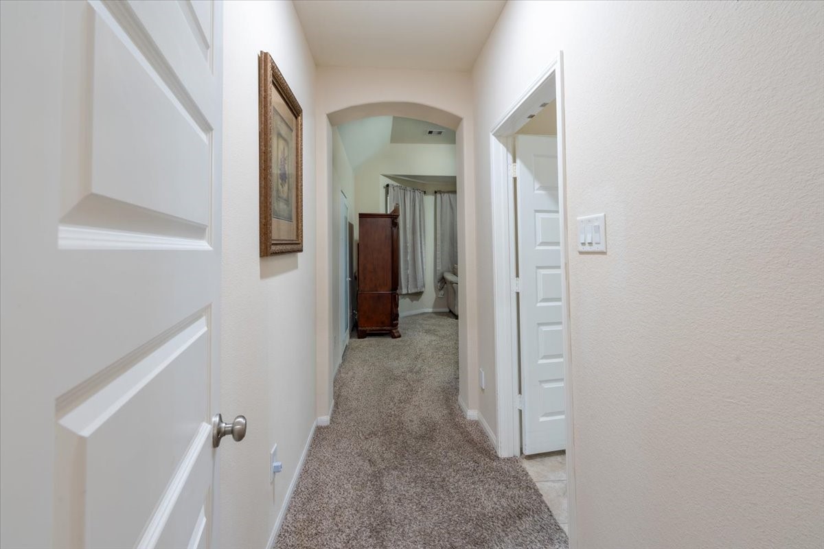 22002 Flashing Ridge Spring, TX 77389 - Photo 14 of 43 This photo shows a hallway with carpeted flooring, light-colored walls, and an arched entryway leading to another room. There are doors on both sides and a framed picture on the wall.