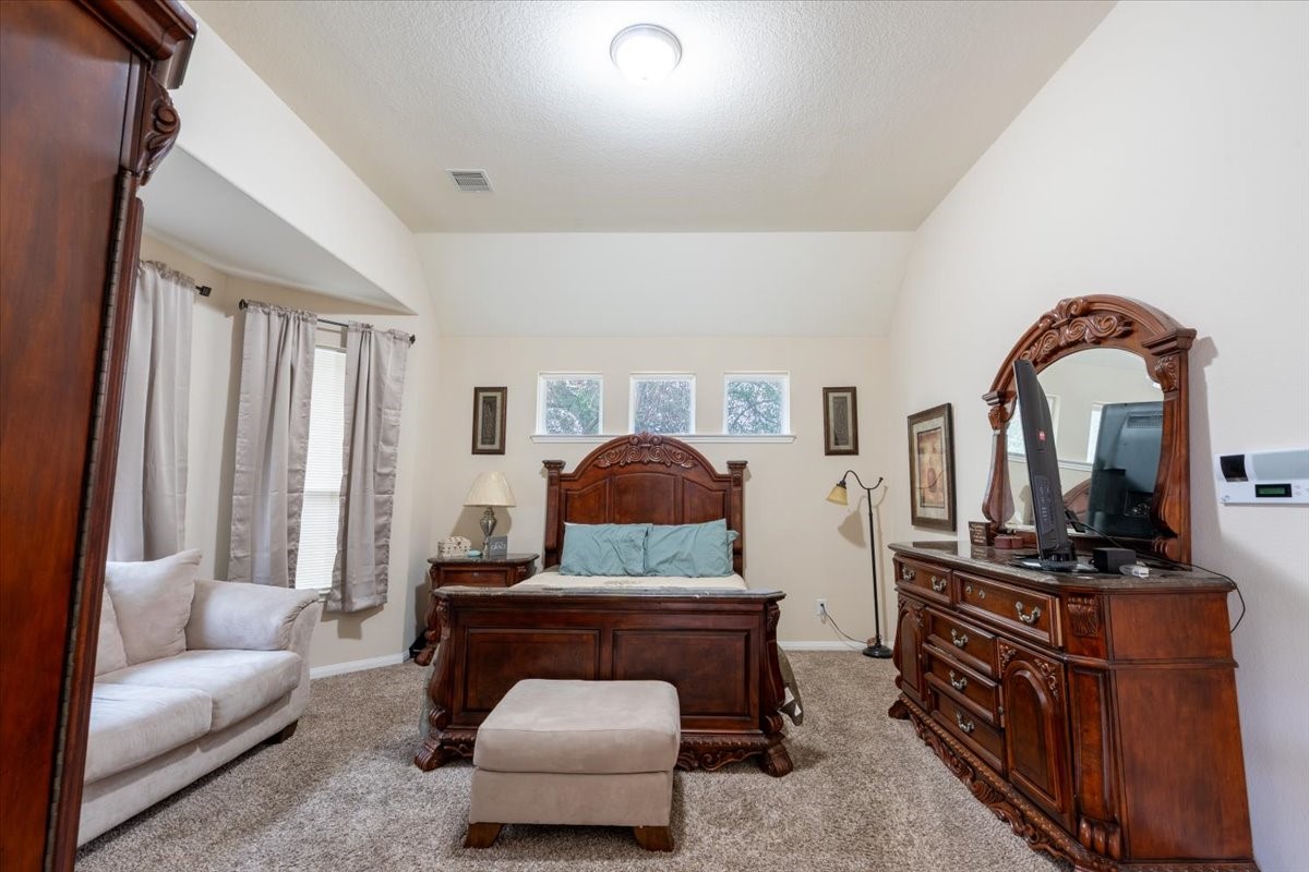 22002 Flashing Ridge Spring, TX 77389 - Photo 16 of 43 Spacious bedroom with elegant wooden furniture, including a bed, dresser, and nightstand. Features a cozy seating area, carpeted floor, and ample natural light through multiple windows.