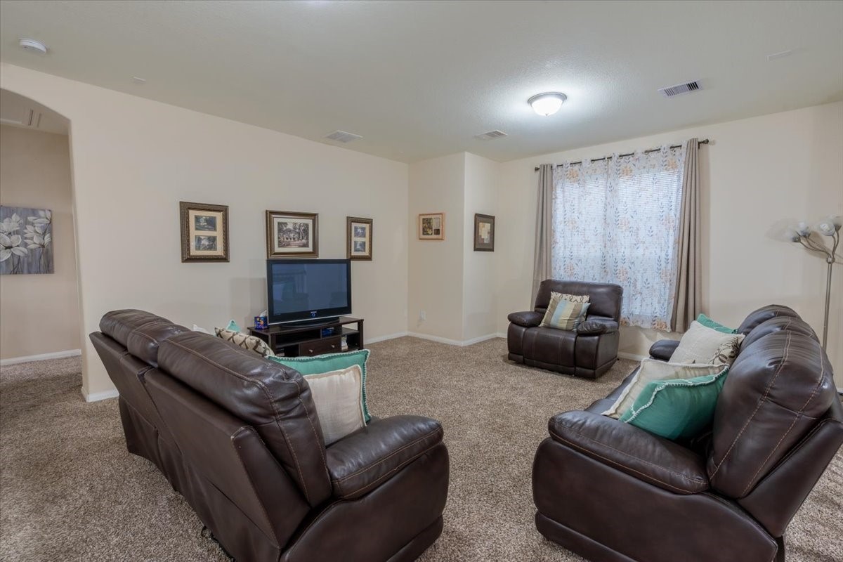 22002 Flashing Ridge Spring, TX 77389 - Photo 24 of 43 This cozy living room features plush brown leather sofas, a TV setup, and carpeted flooring. Neutral walls are adorned with framed art, and a large window with curtains provides natural light. Perfect for relaxation.