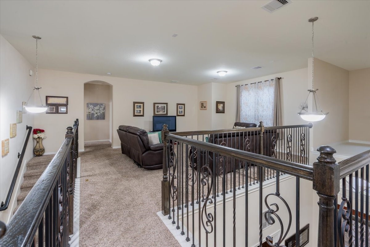 22002 Flashing Ridge Spring, TX 77389 - Photo 25 of 43 This photo showcases a spacious, carpeted upper-level living area with elegant wrought iron railing. The space is well-lit with modern pendant lights, features comfortable seating, and has decorative wall art, creating a cozy, inviting atmosphere.