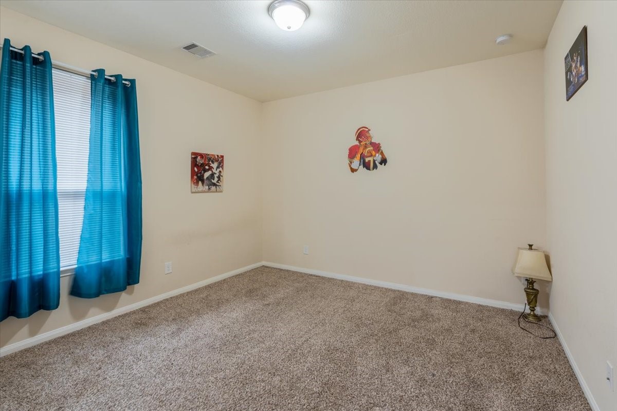 22002 Flashing Ridge Spring, TX 77389 - Photo 30 of 43 This room features neutral walls, carpeted flooring, and a bright window with blue curtains. It has minimal decor and a ceiling light, providing a cozy, versatile space.