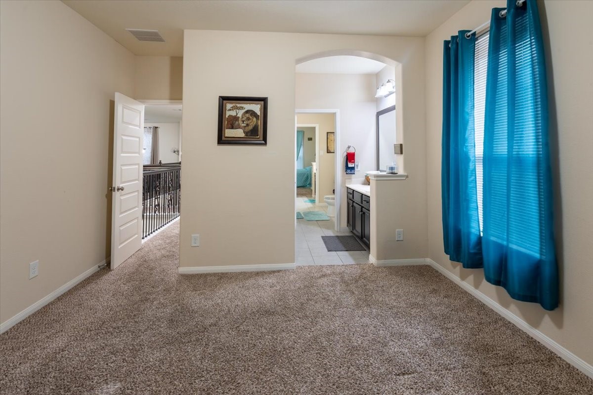 22002 Flashing Ridge Spring, TX 77389 - Photo 32 of 43 This is a cozy, carpeted room with neutral walls and an open layout. It features an archway leading to a bathroom with a double vanity, and a window with blue curtains providing natural light.