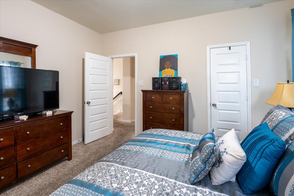 22002 Flashing Ridge Spring, TX 77389 - Photo 34 of 43 This bedroom features cozy carpeting, a large bed with blue and gray bedding, and two wooden dressers. It has neutral walls, a mounted TV, and ample natural light. A doorway leads to a hallway, and there's a colorful piece of art above one dresser.