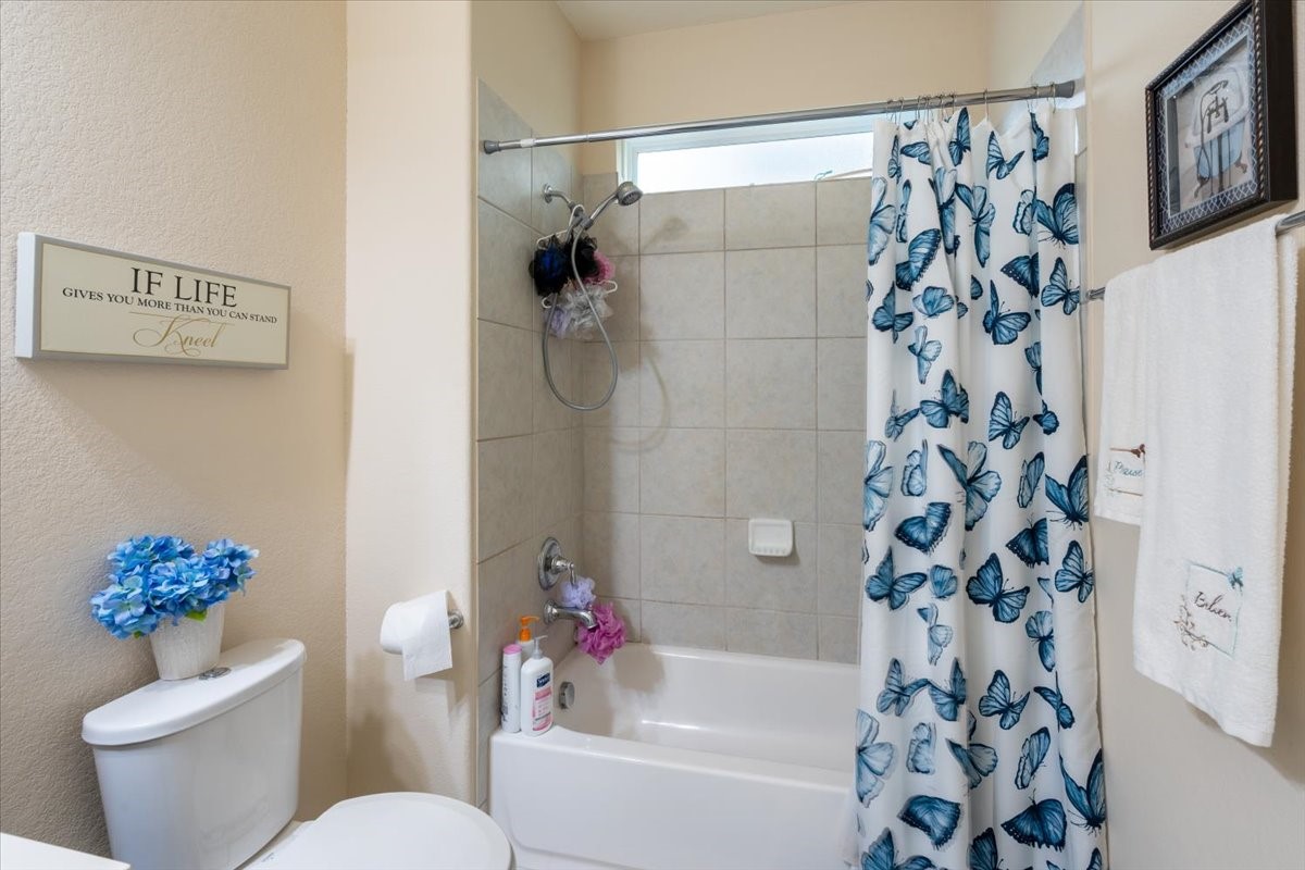 22002 Flashing Ridge Spring, TX 77389 - Photo 36 of 43 This is a cozy bathroom featuring a tiled shower-tub combo with a butterfly-themed curtain. The space includes a toilet with decorative flowers and framed wall art, adding a touch of charm and personality.