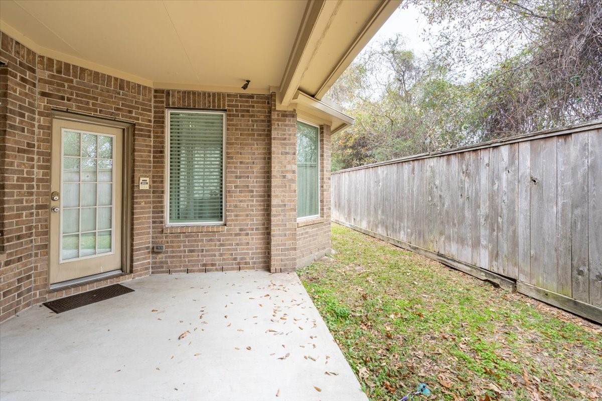 22002 Flashing Ridge Spring, TX 77389 - Photo 38 of 43 This photo showcases a cozy backyard patio area with a covered space, brick exterior, and a wooden fence providing privacy. Ideal for outdoor relaxation or small gatherings.