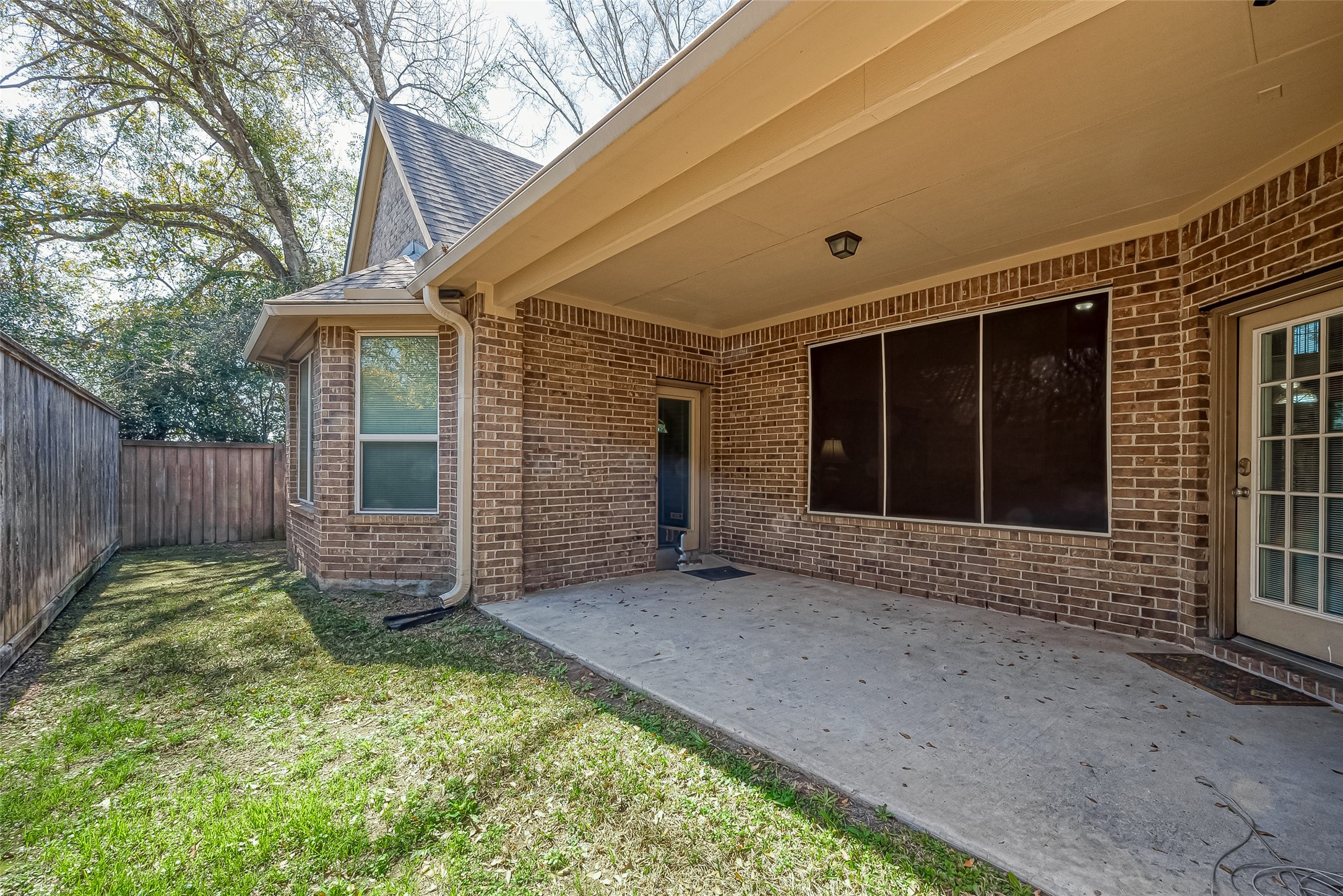 22002 Flashing Ridge Spring, TX 77389 - Photo 39 of 43 This photo showcases a covered brick patio area with a concrete floor, offering a cozy outdoor space. It's bordered by a wooden fence and adjacent to a lawn, providing privacy and a peaceful setting. The area is partially shaded by trees, enhancing the outdoor ambiance.