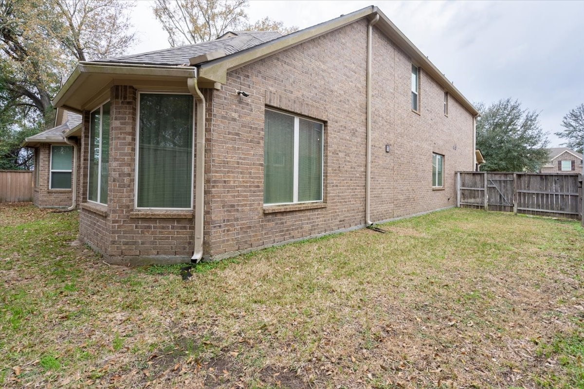 22002 Flashing Ridge Spring, TX 77389 - Photo 41 of 43 This photo shows the exterior of a two-story brick house with a fenced backyard. The yard is grassy with some fallen leaves, and the home features large windows and a sloped roof.