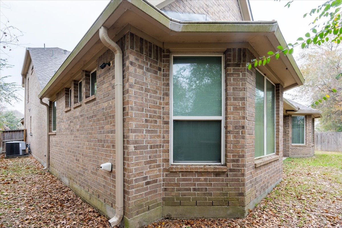 22002 Flashing Ridge Spring, TX 77389 - Photo 42 of 43 This photo shows a brick exterior of a home with large windows and a sloped roof. The yard is covered with fallen leaves, and the property is lined with a wooden fence, providing privacy.