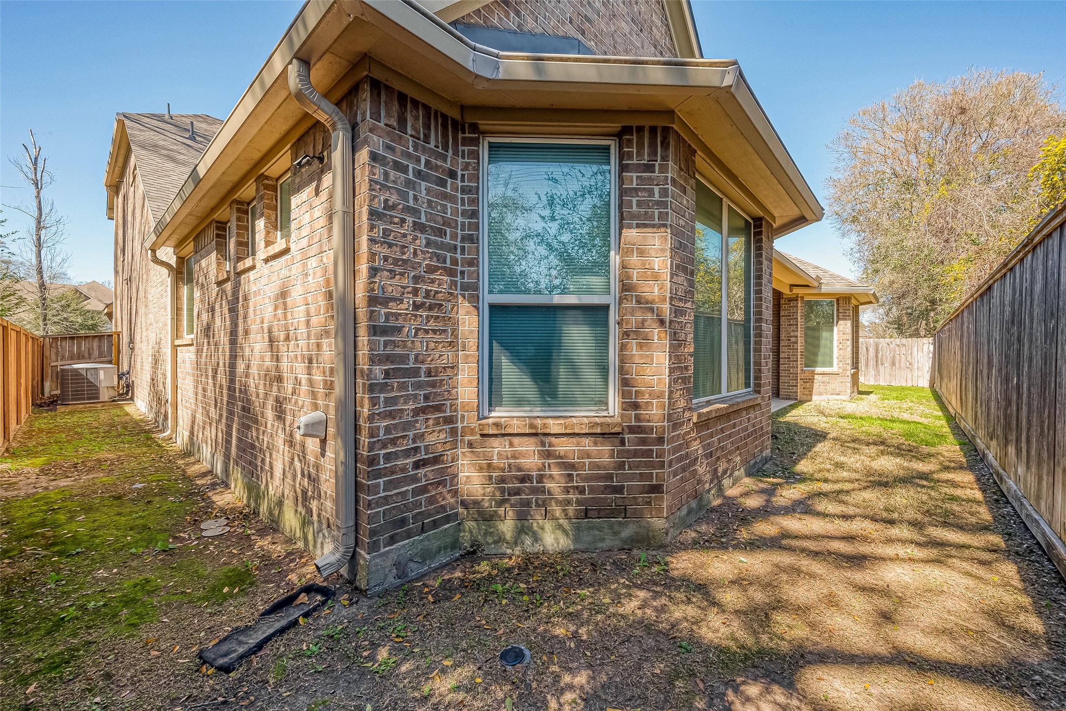 22002 Flashing Ridge Spring, TX 77389 - Photo 43 of 43 This photo shows the exterior side of a brick home with large windows, a narrow side yard, and a wooden fence. The area is partially shaded, with grass and some mossy patches.