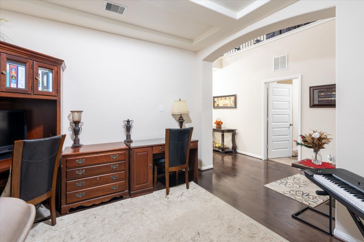 22002 Flashing Ridge Spring, TX 77389 - Photo 5 of 43 This photo showcases a bright home office with elegant wood furniture, including a desk and shelving. The room features dark hardwood floors and opens to a hallway with a decorative console table. A keyboard adds a musical touch, while recessed lighting and an archway enhance the spacious feel.