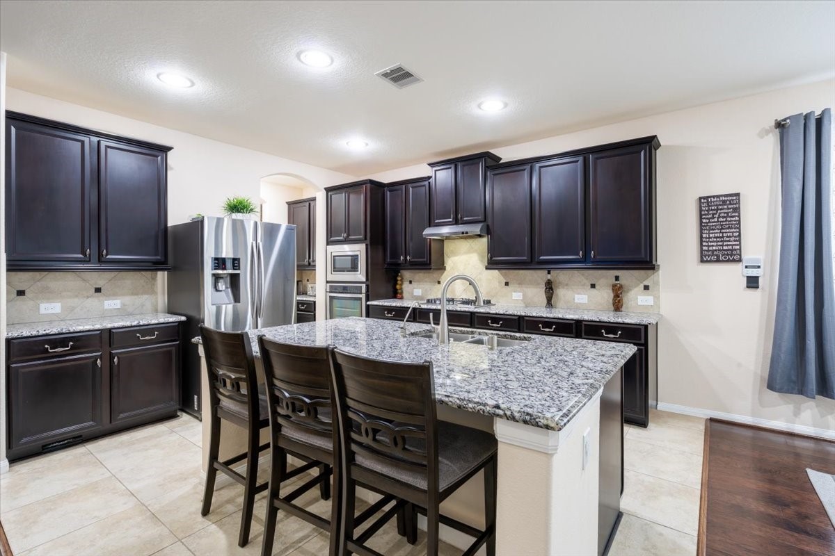 22002 Flashing Ridge Spring, TX 77389 - Photo 8 of 43 Modern kitchen with dark cabinetry and granite countertops. Features a large island with seating, stainless steel appliances, and tile flooring. Bright and spacious with recessed lighting.
