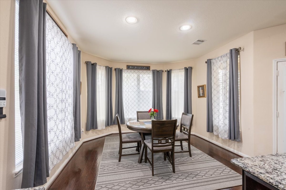 22002 Flashing Ridge Spring, TX 77389 - Photo 10 of 43 Bright dining area with large windows, elegant drapes, and hardwood floors. Features a round table with chairs and a cozy rug, creating a welcoming atmosphere.
