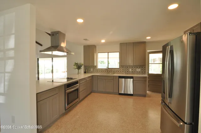 a kitchen with stainless steel appliances granite countertop a refrigerator a sink dishwasher a stove and white countertops with wooden floor