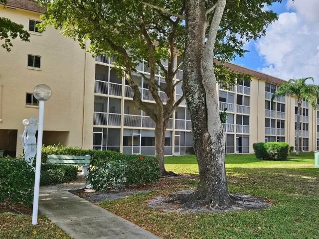 a front view of a building with a garden and trees