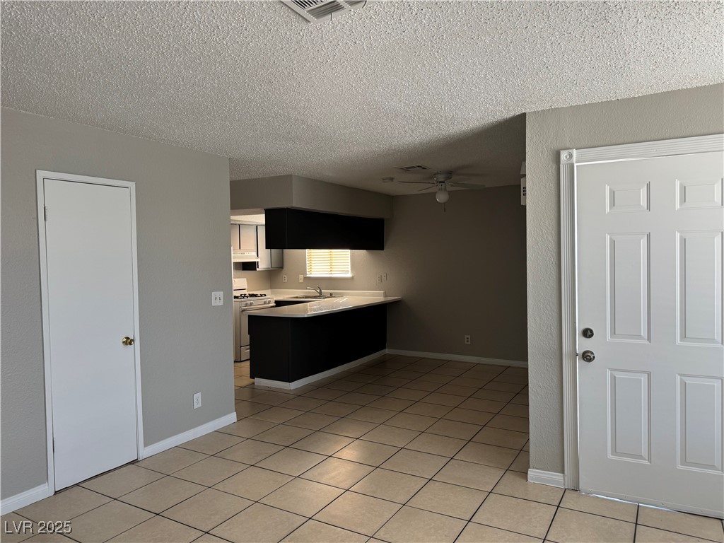 6925 Hopkins Drive, Unit 4 Las Vegas, NV 89156 - Photo 2 of 12 Kitchen with light countertops, a peninsula, white range with gas cooktop, light tile patterned floors, and a ceiling fan