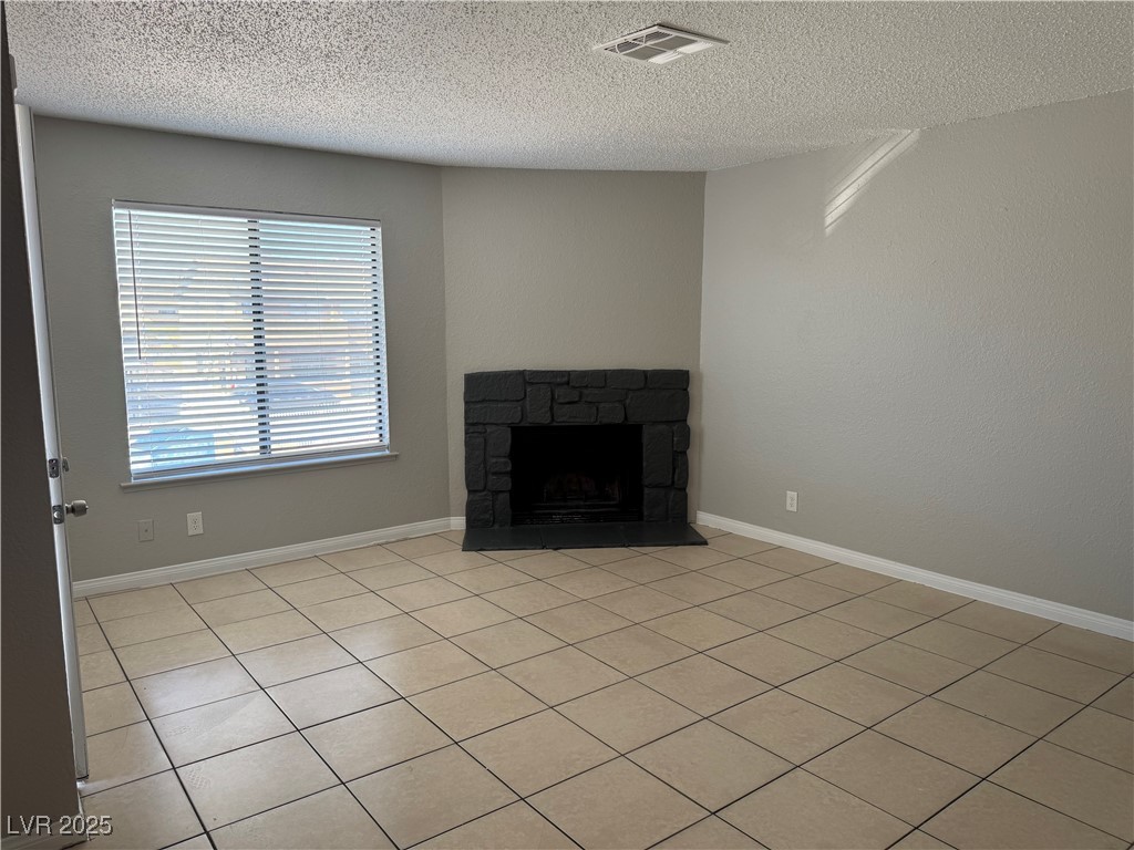 6925 Hopkins Drive, Unit 4 Las Vegas, NV 89156 - Photo 5 of 12 Unfurnished living room featuring light tile patterned floors, a textured ceiling, and a fireplace