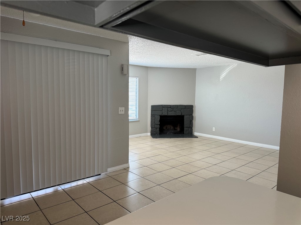 6925 Hopkins Drive, Unit 4 Las Vegas, NV 89156 - Photo 7 of 12 Unfurnished living room with light tile patterned flooring, a stone fireplace, and a textured ceiling