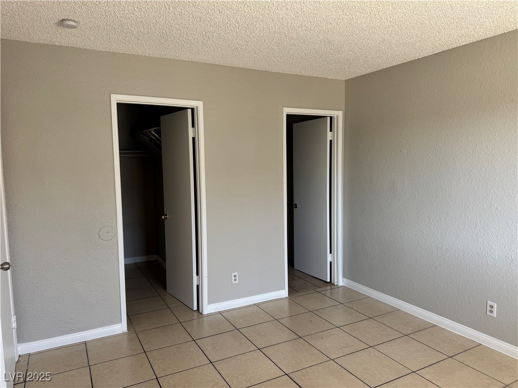 6925 Hopkins Drive, Unit 4 Las Vegas, NV 89156 - Photo 10 of 12 Unfurnished bedroom featuring a textured wall, a textured ceiling, a walk in closet, and light tile patterned floors