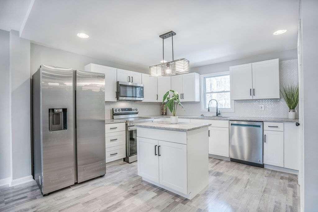 a kitchen with stainless steel appliances granite countertop a refrigerator a stove a sink dishwasher a refrigerator and white cabinets with wooden floor