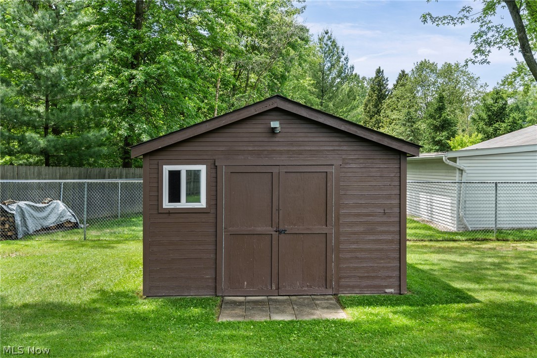 17583 Shurmer Road Strongsville, OH 44136 - Photo 42 of 50 Brown-stained wood-sided shed featuring a white-framed window, double entry doors, a dark shingled roof, and a concrete paver threshold