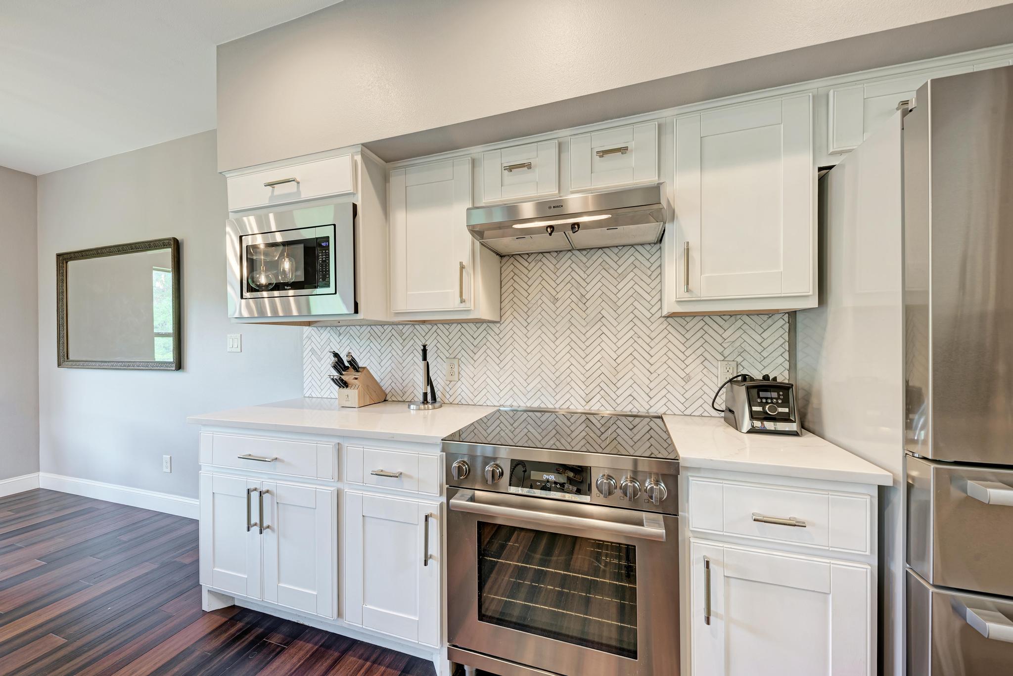 2605 Indian Creek Road Austin, TX 78734 - Photo 9 of 33 Kitchen featuring white shaker cabinetry, stainless steel appliances, a herringbone tile backsplash, quartz countertops, and wood-finish flooring