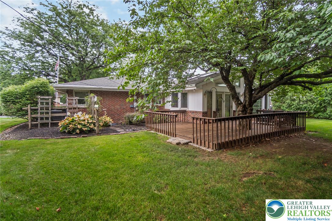 1328 Russett Road Allentown, PA 18104 - Photo 41 of 46 A spacious wooden deck extends from this brick residence, offering ample outdoor living space shaded by a mature tree.