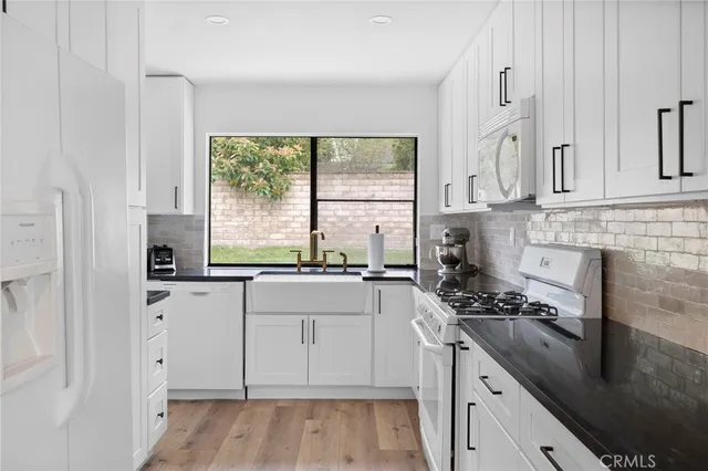 a kitchen with granite countertop a stove a sink and white cabinets