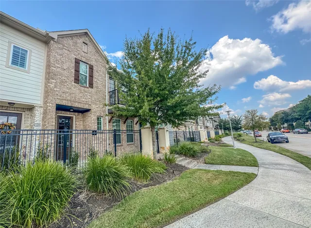 a view of a brick house next to a yard with plants and trees