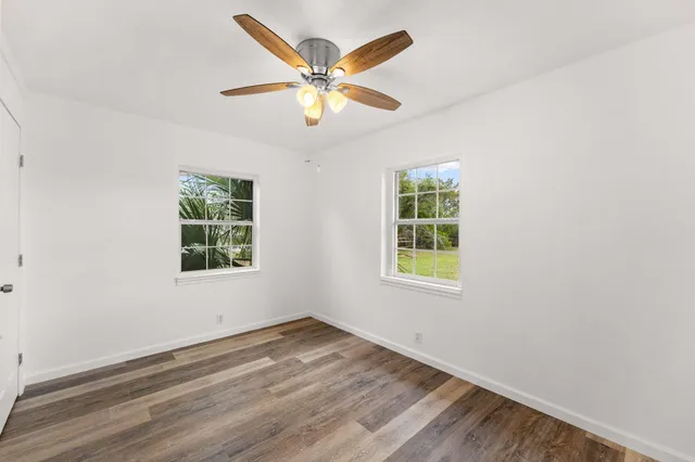 an empty room with wooden floor fan and windows