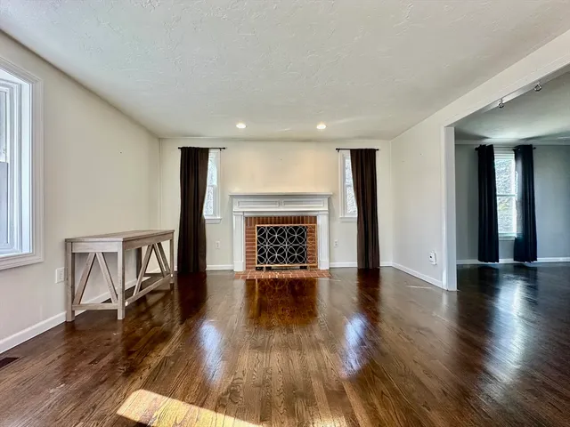 a view of an empty room with wooden floor fireplace and a window
