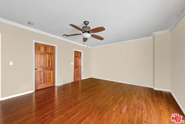 a view of an empty room with wooden floor and a ceiling fan