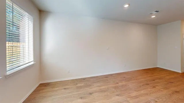a view of an empty room with wooden floor and a window